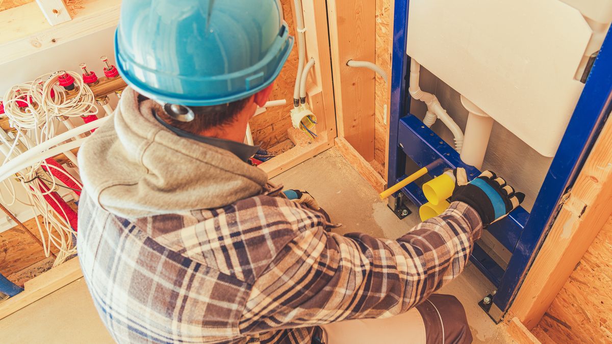Plumber in a hard hat fitting concealed toilet pipework on a construction site