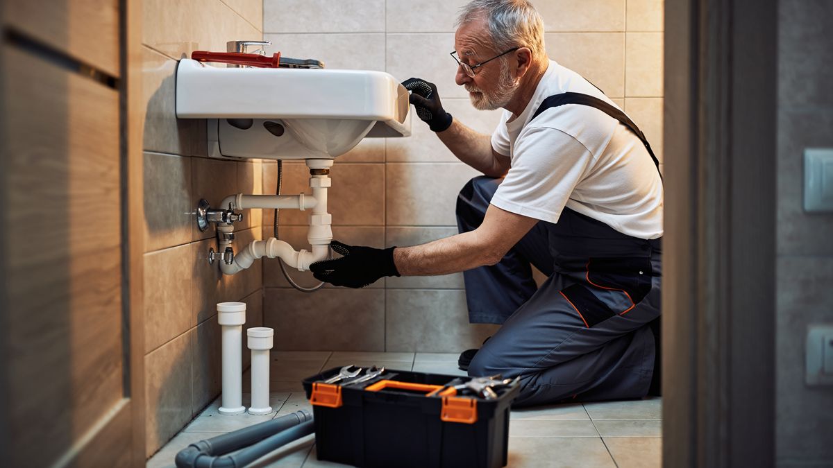 Plumber working on pipework in a modern tiled bathroom