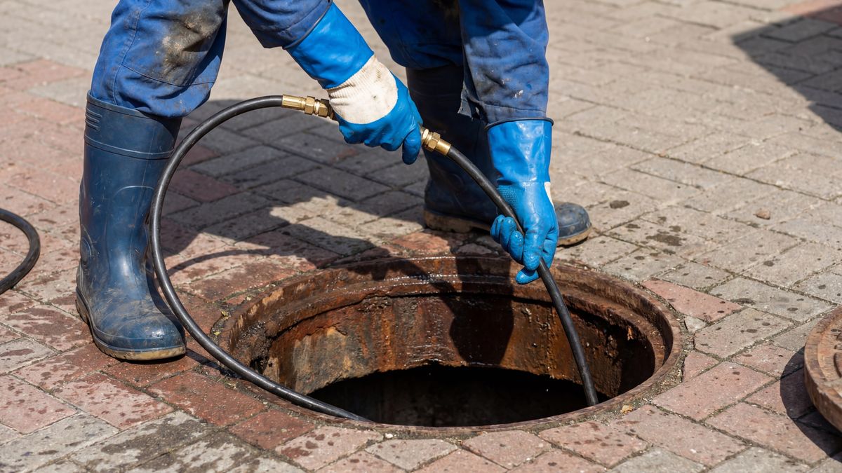 Worker feeding a high-pressure jetting hose down into an open sewer manhole