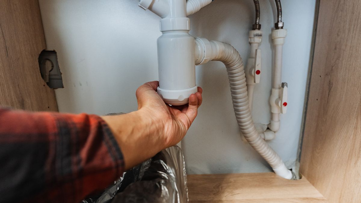 Hand gripping the white P-trap under a sink, ready to remove it