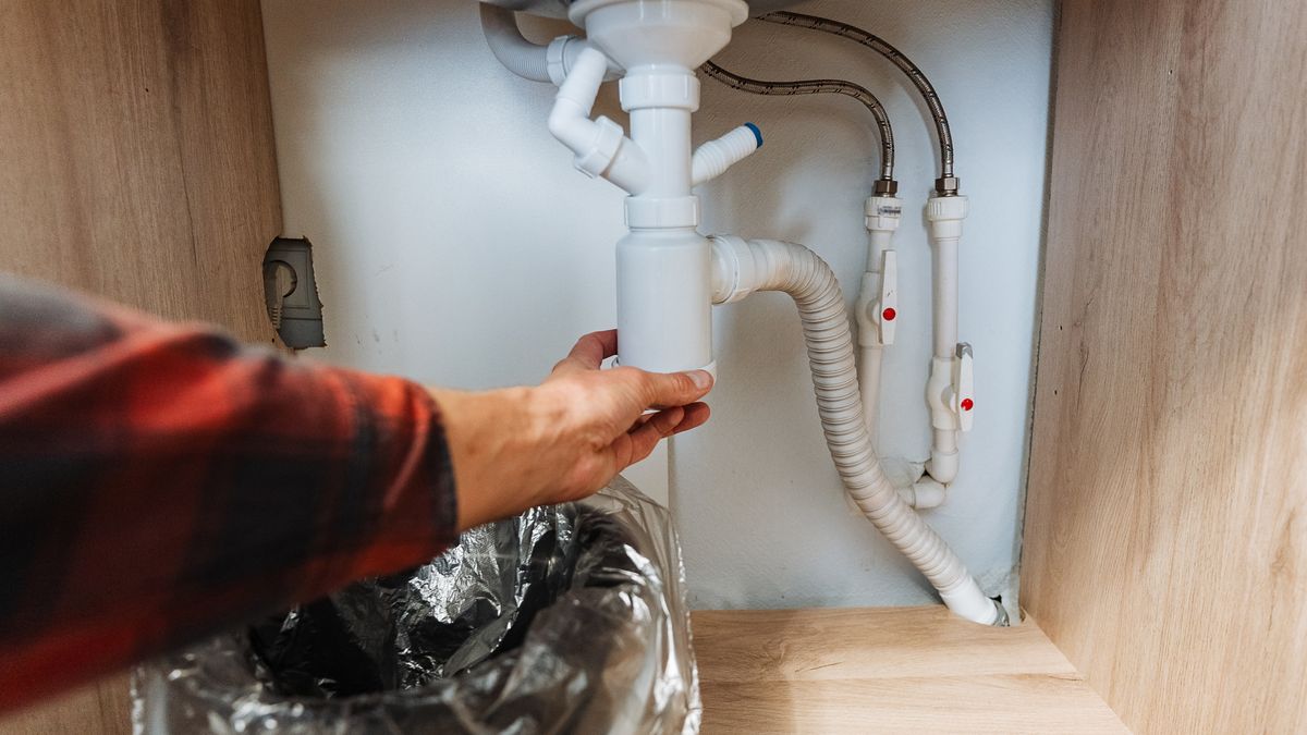 Under-sink pipework with a hand holding the P-trap beside the flexible waste hose