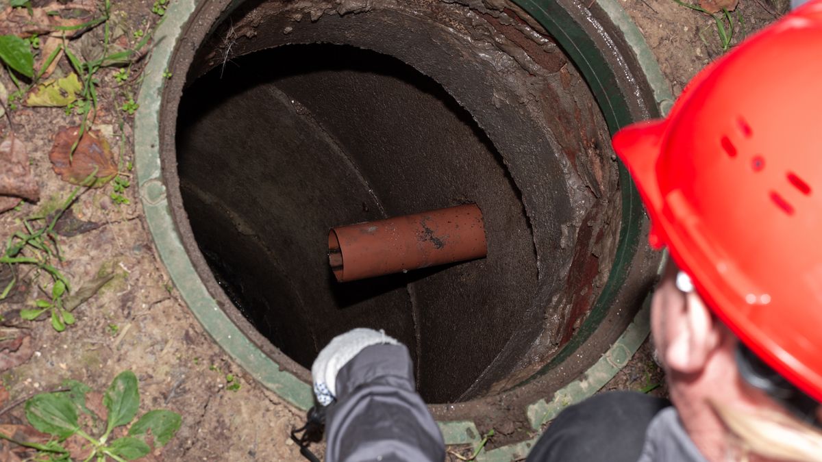 Worker leaning over an open septic tank where the sewage drain pipe enters