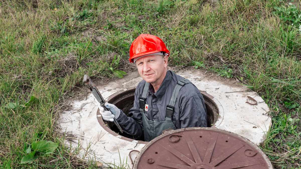 Plumber working down inside an open sewer chamber, looking up from below ground
