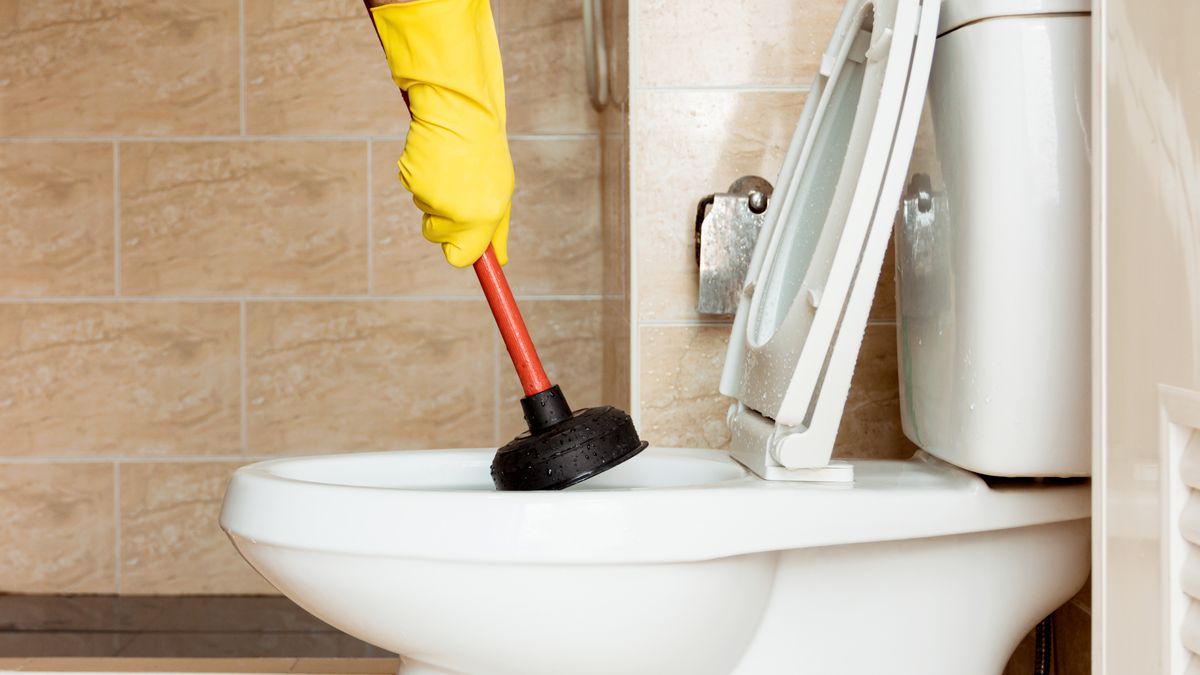 Technician using an auger tool to clear a blocked toilet bowl